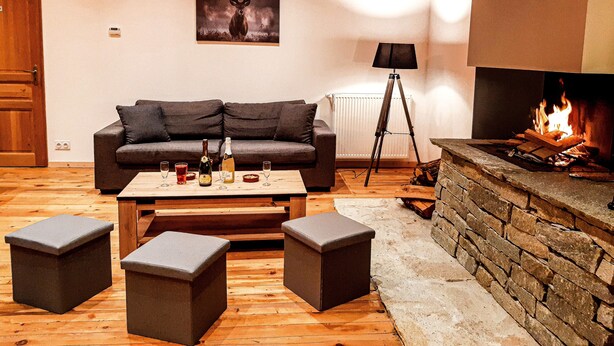 Een knusse woonkamer met een open haard, een bank, een bijzettafeltje en twee poufs.