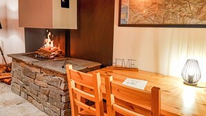 Een stenen openhaard met vuur, een houten tafel met stoelen, en een kaart aan de muur.