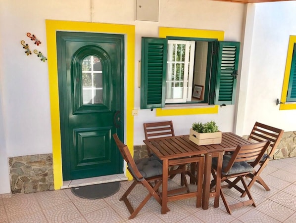 Un coin repas avec une table et des chaises, une porte verte et une fenêtre avec des volets verts.