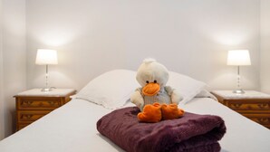Un lit avec un doudou en forme de canard et une couverture violette, flanqué de deux lampes de chevet.