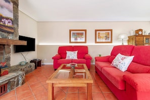 A living room with red sofas, a wooden coffee table, a stone fireplace, and framed artwork on the wall.