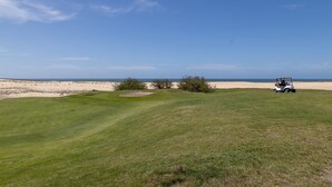 En golfbane med klart skinnende himmel, en sandstrand i baggrunden og en golfvogn.