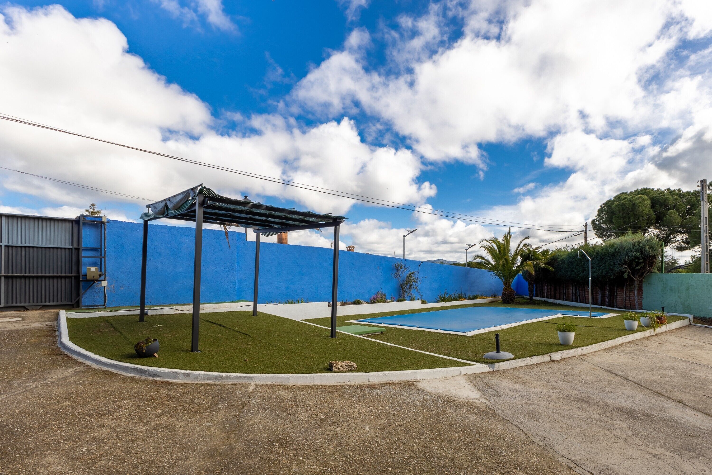 Una piscina en la azotea con un pérgola, una pared azul y cielo despejado.
