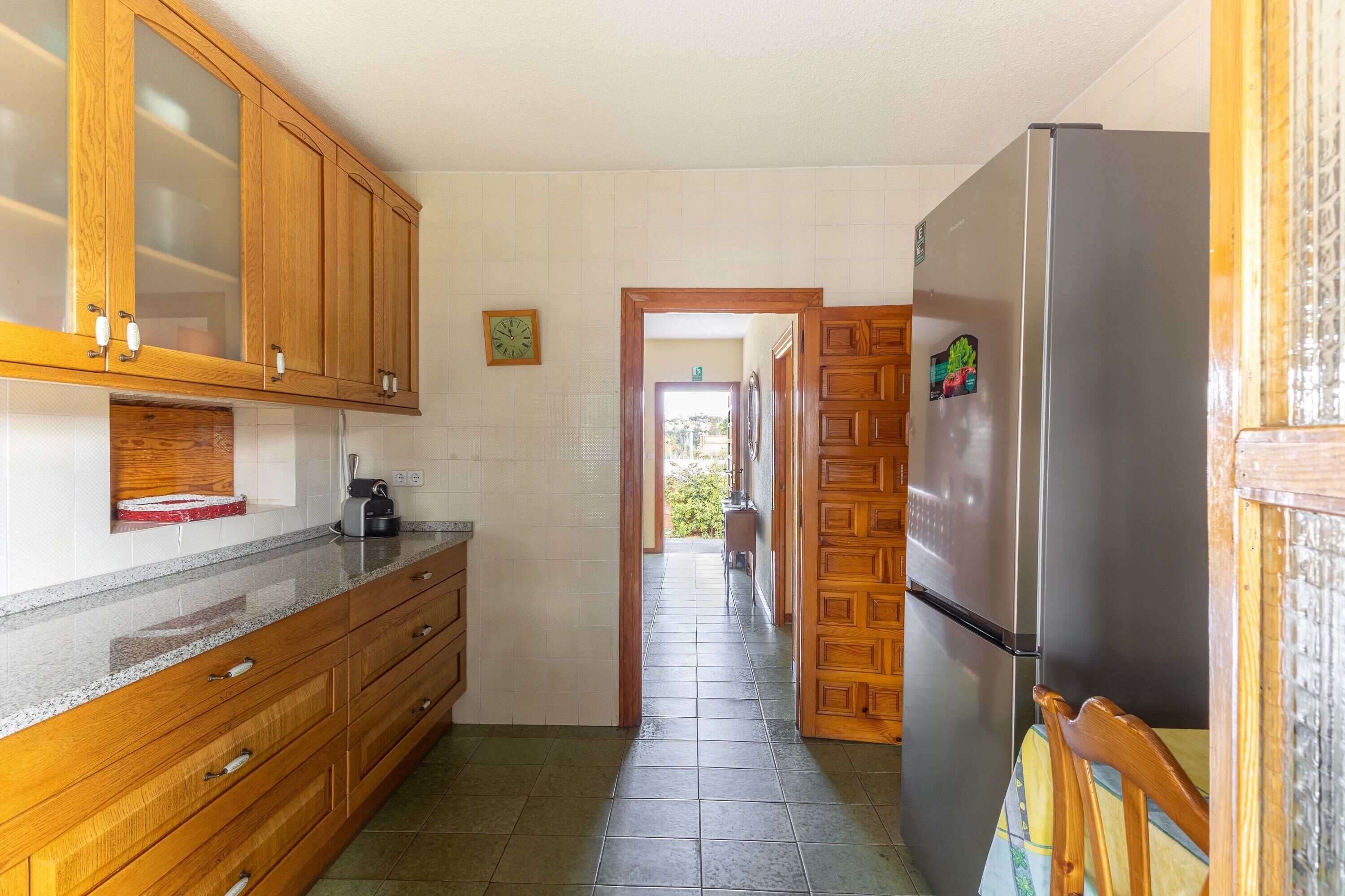 A kitchen with wooden cabinets, a stainless steel refrigerator, and a tiled floor.