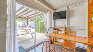 Een kamer met een houten tafel, stoelen, een aan de muur bevestigde televisie en een schuifdeur naar buiten.