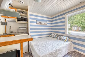 Une chambre avec un lit, un bureau, un four à micro-ondes et une fenêtre donnant sur un espace verdoyant.