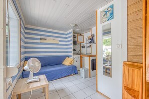 A room with a striped wall, a blue sofa, a fan, a small table, and a wooden cabinet.