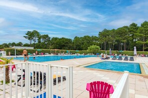 A swimming pool area with multiple pools, lounge chairs, and umbrellas.