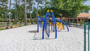 A playground with climbing structures and a sandy play area, surrounded by trees and a fence. - Apartment 'Chalet B Village Vacances' with Shared Pool, Private Terrace and Wi-Fi (Gujan-Mestras)