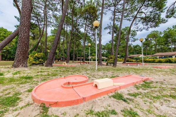 A park with a red play structure, trees, and benches.