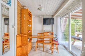 A compact room with a wooden cabinet, a dining table with chairs, a television, and a sliding glass door to the outside.