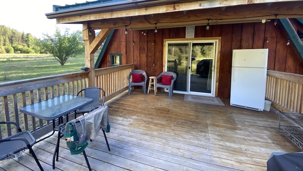 Eine Holzhütte mit einer Terrasse, einem Tisch, Stühlen und einem Kühlschrank.