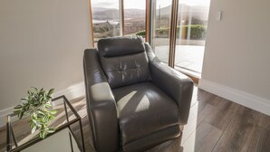 A modern living room with a leather sofa, a glass coffee table, and a view of a mountainous landscape through large sliding glass doors.