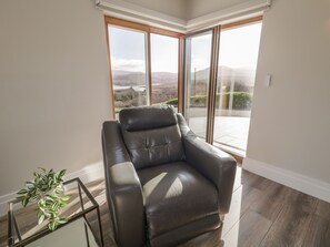 Ein modernes Wohnzimmer mit einer Ledersofa, einem Glastisch und Blick auf eine gebirgige Landschaft durch große Schiebeglastüren.