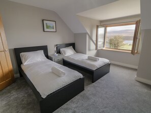 A bedroom with two beds, a nightstand, a bedside table, a framed picture on the wall, and a window with a view.