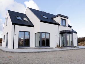 A modern two-story house with large windows, a sloped roof, and a gravel driveway.