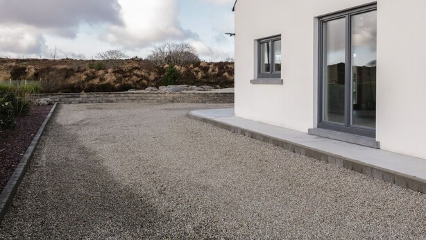 A modern building with a gravel driveway and a landscaped area with shrubs.