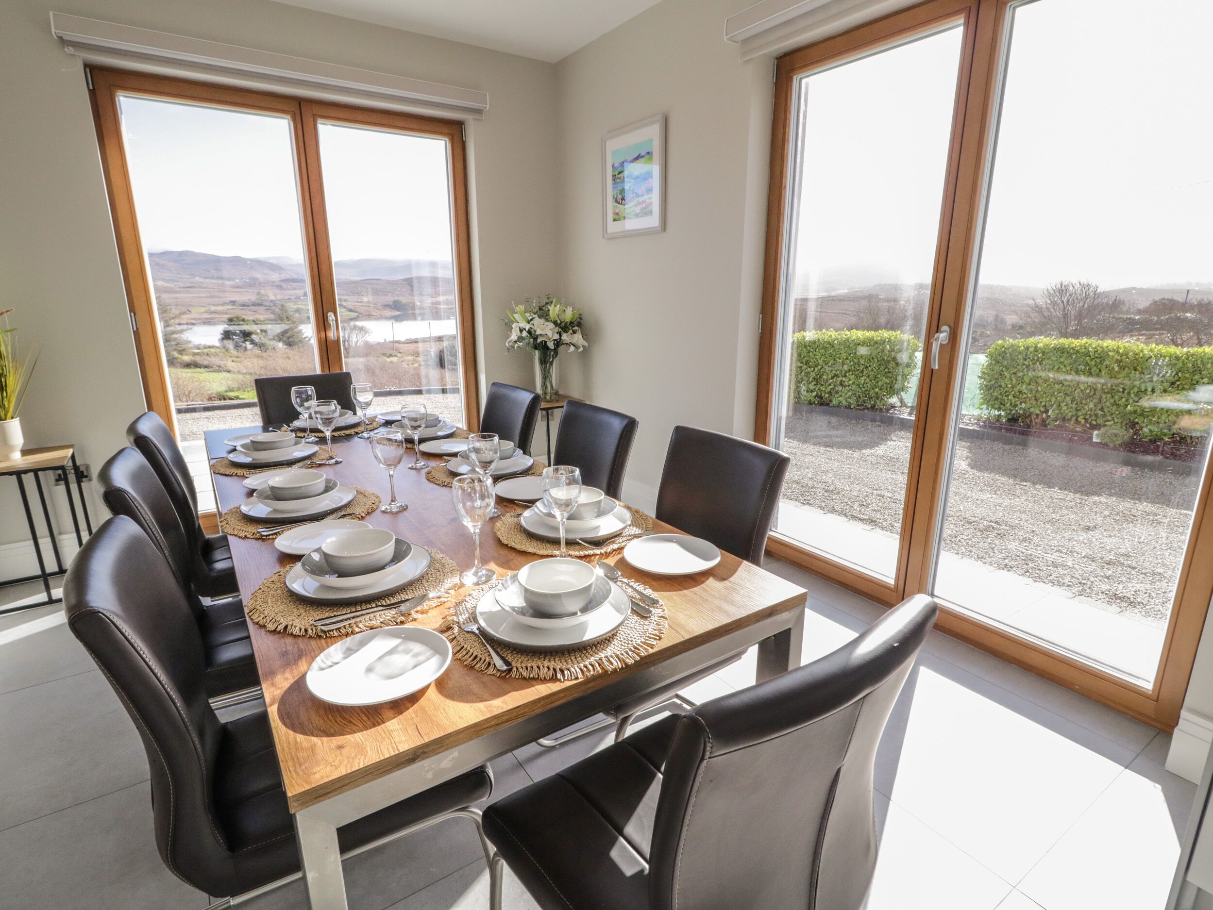 A dining area with a table set for six, large windows, and a view of the countryside.