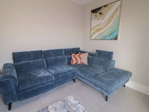 A blue sectional sofa with a patterned throw pillow, a blue rug, and a marble wall art piece.
