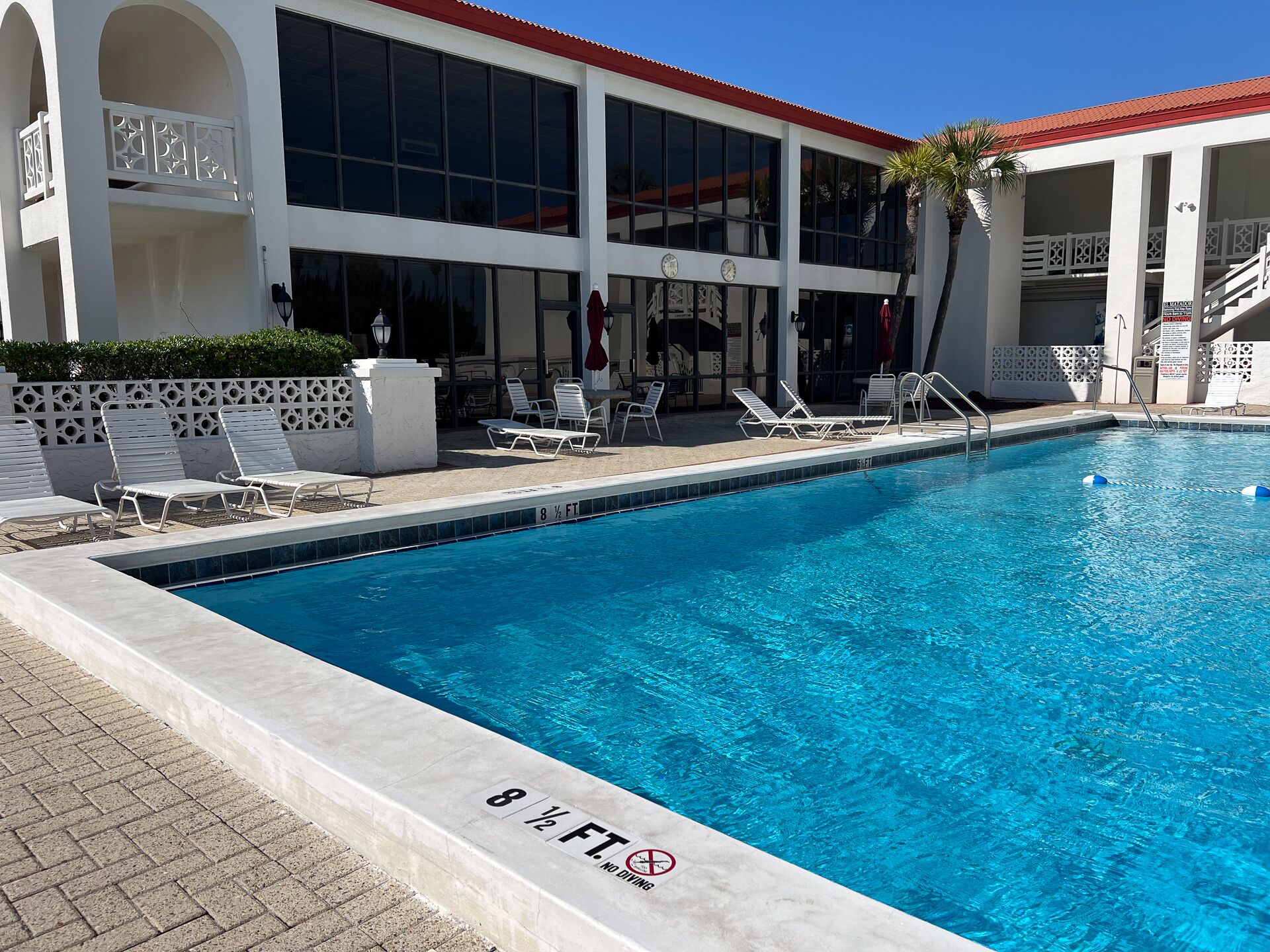 Piscina com espreguiçadeiras e um edifício com janelas amplas e telhado vermelho.