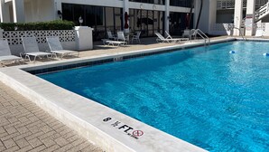 Une piscine avec des chaises longues et un bâtiment doté de grandes fenêtres et d’un toit rouge.