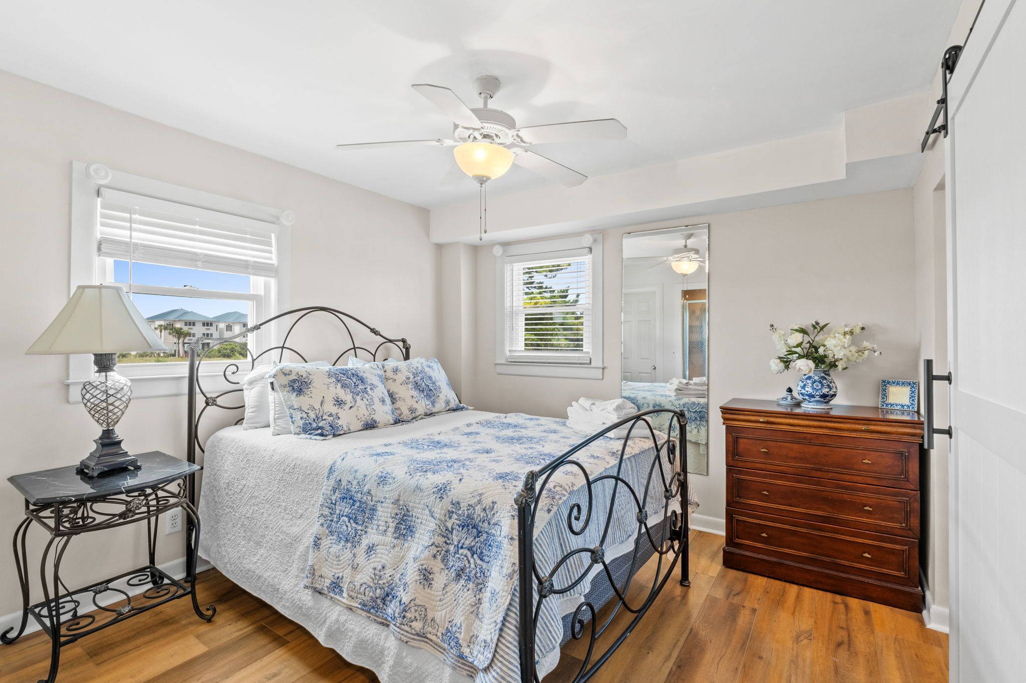 A bedroom with a bed, a dresser, a nightstand, a ceiling fan, and a window with blinds.