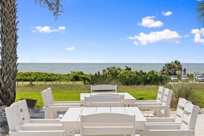Un espace aménagé avec des tables et des chaises blanches, un palmier et une vue sur l’océan, situé au bord de la plage.
