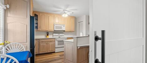 Cocina compacta con armarios de madera, microondas, horno y ventilador de techo.