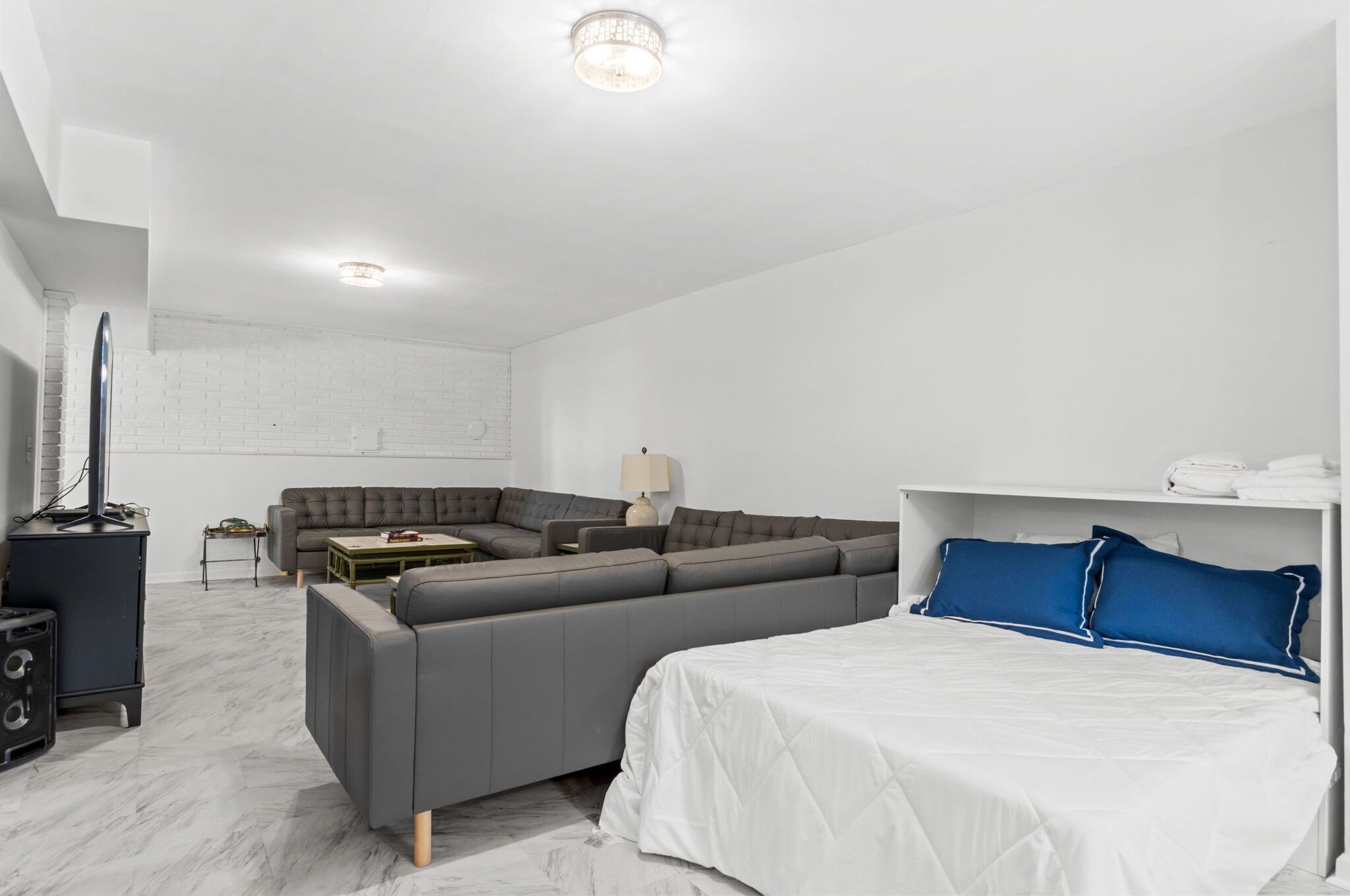 A modern, minimalist bedroom with a large bed, grey sofa, and a small table.