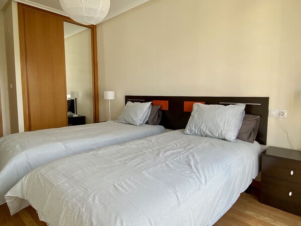 A double bed with a wooden headboard, two bedside tables, and a nightstand. - Apartment with ocean views and community pool, just a 3 min walk to the beach! (O Porto de Espasante)