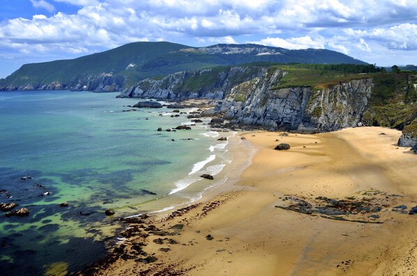 Un paysage côtier avec une plage de sable, des falaises rocheuses et une montagne en arrière-plan.