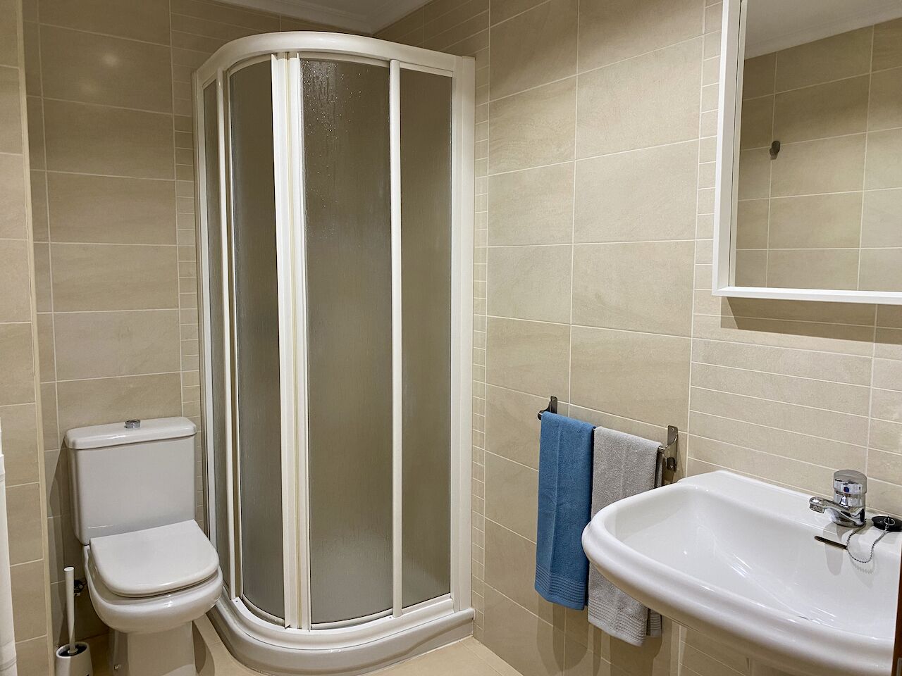 Un bagno con box doccia, wc, lavandino e porta asciugamani.