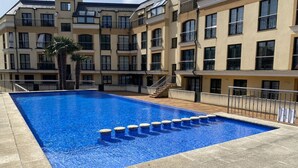 A swimming pool with a tiled deck, surrounded by a multi-story building with balconies. - Apartment with ocean views and community pool, just a 3 min walk to the beach! (O Porto de Espasante)