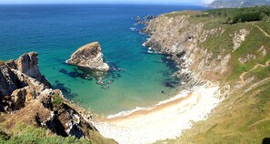 A coastal landscape with a rocky cliff, clear blue sea, and a sandy beach. - Apartment with ocean views and community pool, just a 3 min walk to the beach! (O Porto de Espasante)