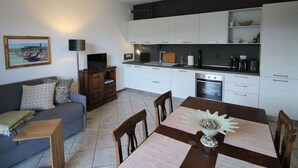 Una cucina moderna con mobili bianchi, un tavolo da pranzo con sottopiatti, un tavolino in legno, un divano con cuscini decorati e un quadro appeso al muro.
