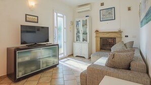 A living room with a flat-screen TV on a cabinet, a sofa, a fireplace, and a glass cabinet with decorative items. - Nice apartment for 4 people with WIFI, A/C, TV and patio (Capanne-prato-cinquale)