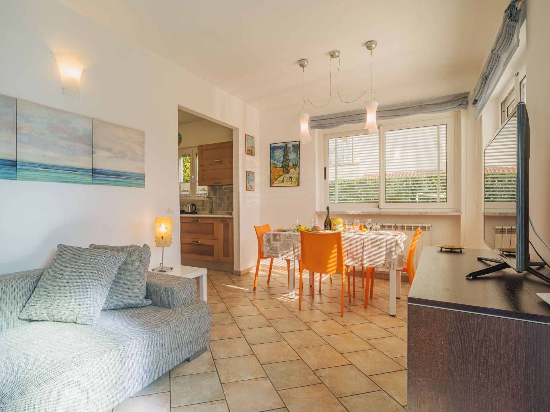 Ein modernes Wohnzimmer mit einer Couch, einem Esstisch und Stühlen. Im Hintergrund ist eine Küche zu sehen.