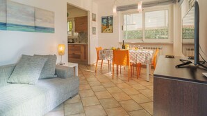 A modern living room with a sofa, dining table, and chairs. There is a kitchen visible in the background. - Nice apartment for 4 people with WIFI, A/C, TV and patio (Capanne-prato-cinquale)