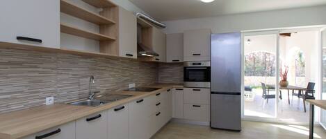 A modern kitchen with a built-in oven, a stainless steel refrigerator, and a wooden countertop.