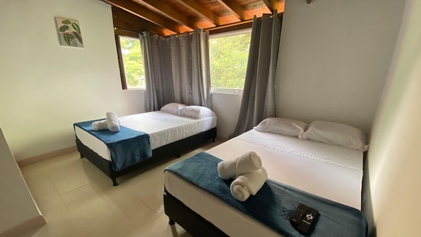 A hotel room with two beds, each with a blue bedspread and white pillows, and a small table with a remote control. - Gold Stadium (Medellín)