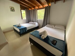 A hotel room with two beds, each with a blue bedspread and white pillows, and a small table with a remote control.