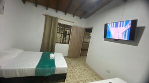 A bedroom with a bed, a television mounted on the wall, a door, and a window.