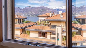 A view from a window overlooking a residential area with terraced houses, a lake, and snow-capped mountains in the background.