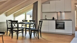 A modern kitchen with white cabinets, a built-in oven, and a dining area with a table and chairs.