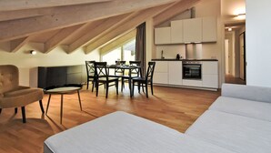 A modern loft apartment with a dining area, kitchen, and a large window providing natural light.