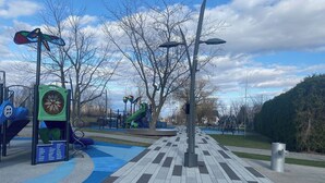 A park with playground equipment, a blue and gray patterned walkway, and a sign indicating 'Parc Francis-Xavier-Fontaine 600 m - 2 min'. - Newly built condo, with excellent natural light, 20 minutes from the airport. (Sainte-Catherine)