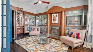 A living room with a fireplace, a glass coffee table, a sofa, and a bookshelf filled with decorative items. - Historic Shaw Home • Sleeps 14 • Near Zoo & Arch (St. Louis)