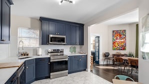 A modern kitchen with dark blue cabinets, stainless steel appliances, and a white marble backsplash. - Historic Shaw Home • Sleeps 14 • Near Zoo & Arch (St. Louis)