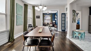 A dining area with a long wooden table and black chairs, green curtains, and a chandelier. - Historic Shaw Home • Sleeps 14 • Near Zoo & Arch (St. Louis)