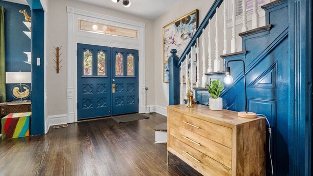 A wooden dresser with drawers, a blue door with glass panels, and a staircase with white balusters. - Historic Shaw Home • Sleeps 14 • Near Zoo & Arch (St. Louis)